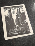 A black and white linocut art print depicting a dramatic canyon scene with a boat on the water, displayed on a dark textured surface.