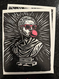 A black and white linocut art print featuring a bust of a Roman-style figure wearing red sunglasses and blowing a pink bubblegum bubble, displayed on a dark textured surface.