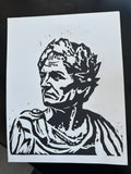 A black and white linocut or woodblock-style portrait print of an ancient Roman bust, shown on a white sheet of paper against a dark background.