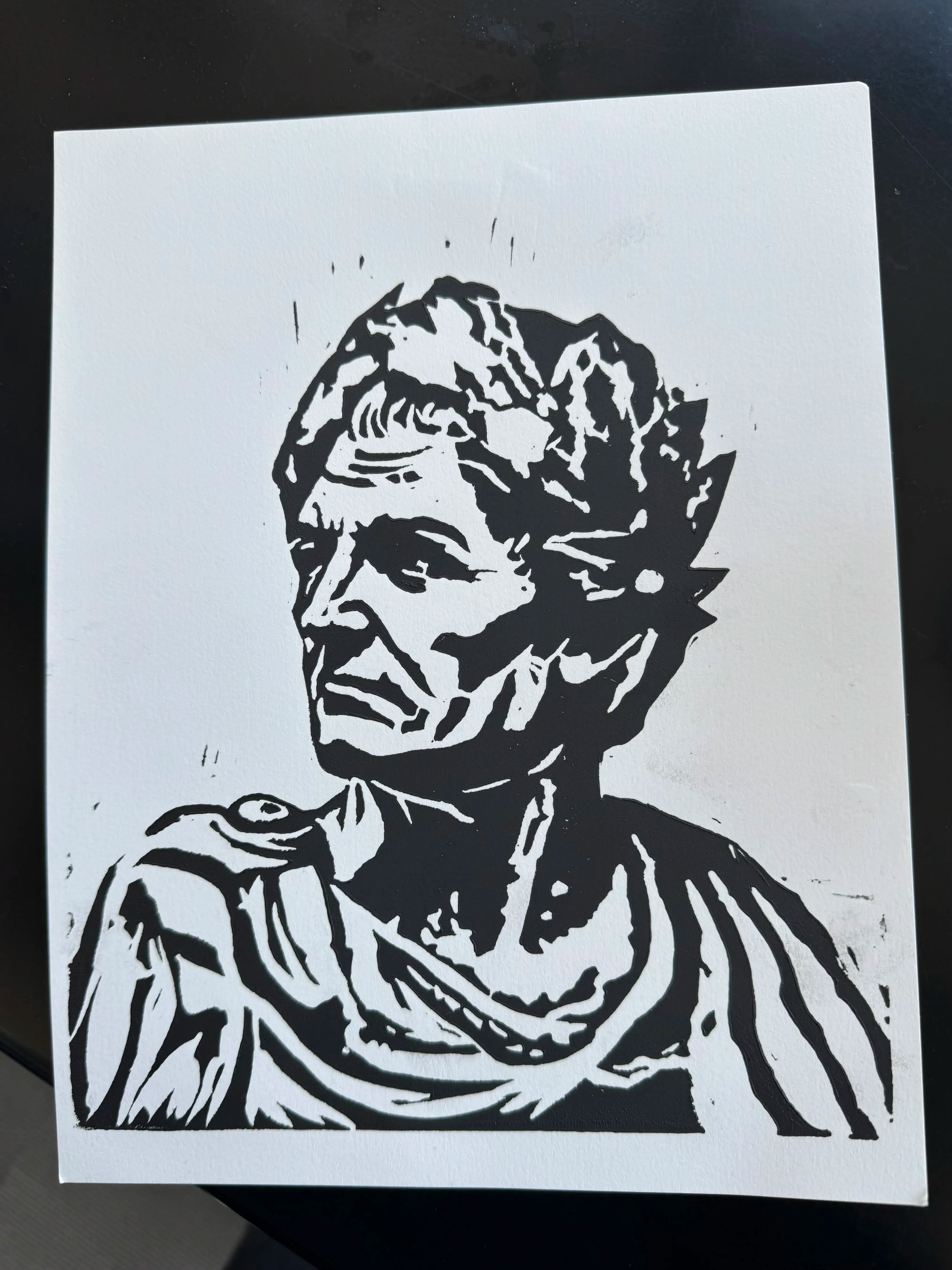 A black and white linocut or woodblock-style portrait print of an ancient Roman bust, shown on a white sheet of paper against a dark background.