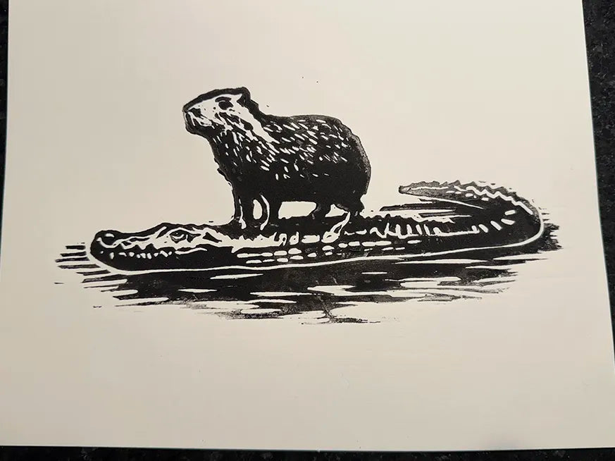 A black ink illustration of a Capybara standing on a crocodile, printed on a white sheet of paper.