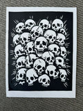 A black and white art print featuring a dense cluster of skulls with radiating lines, presented on a textured gray carpet.
